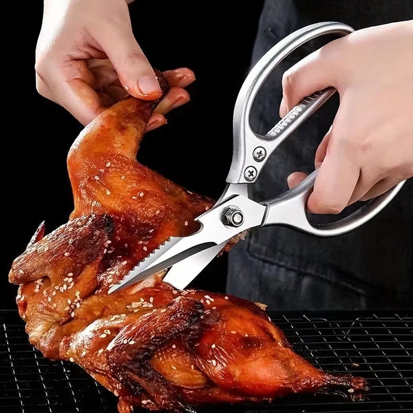 Hände benutzen schwere Küchenschere, um gegrillte Hähnchenflügel auf einem Rost zu schneiden.