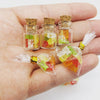 Eine Hand hält mehrere klare Glasfläschchen mit farbigen getrockneten Kräutern oder Blumen und Korkverschluss.