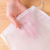 Una mano sostiene una bolsa coladora de malla reutilizable transparente hecha de tela blanca sobre una superficie de madera.