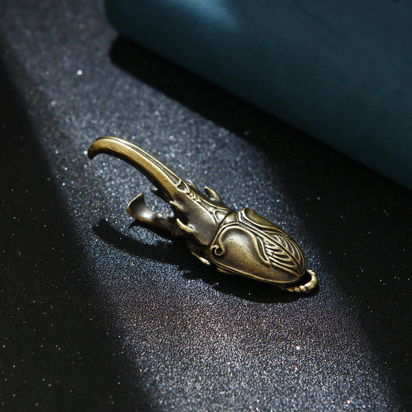 A brass artisan scarab beetle bottle opener resting on a dark, textured surface.