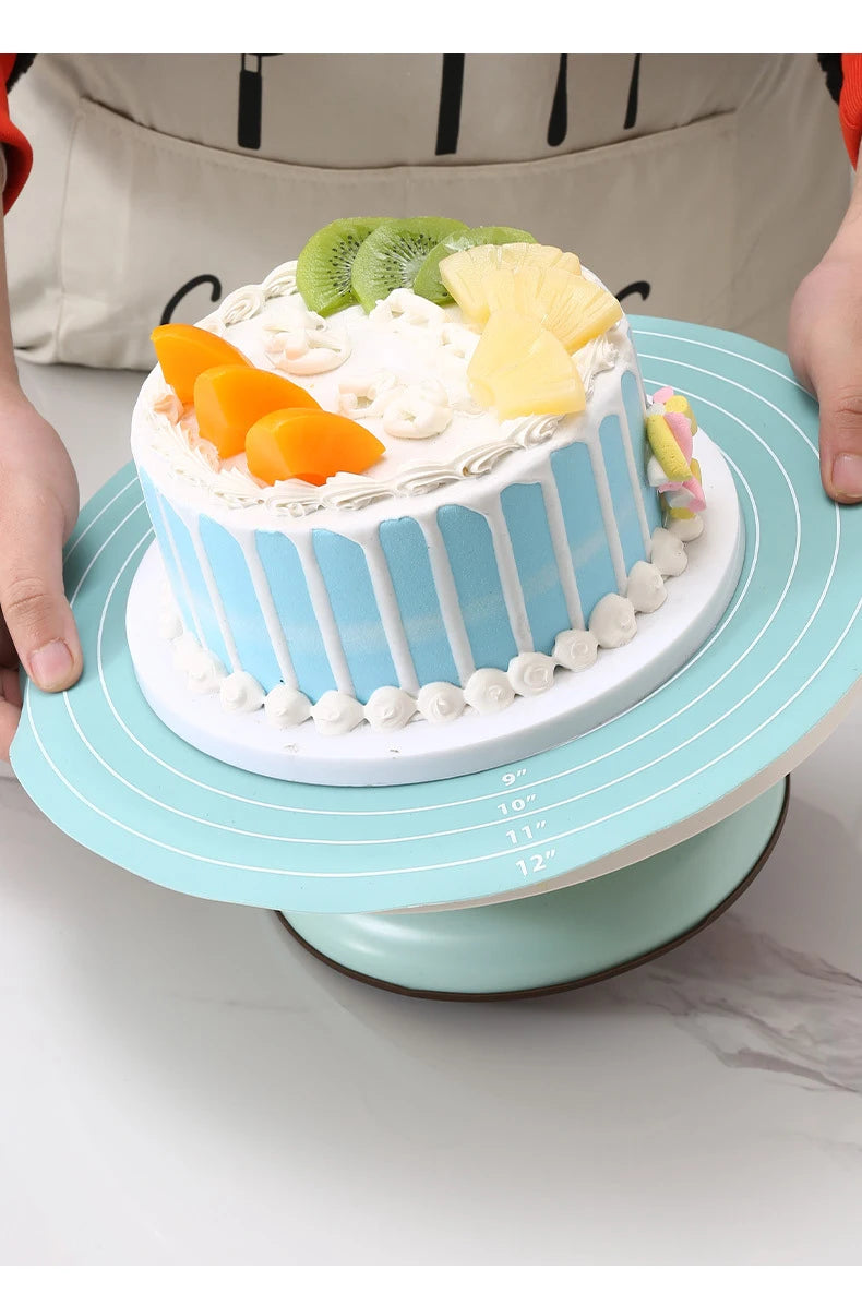 A light blue silicone cake turntable baking mat is shown with a decorated cake and fruit on a white platter.
