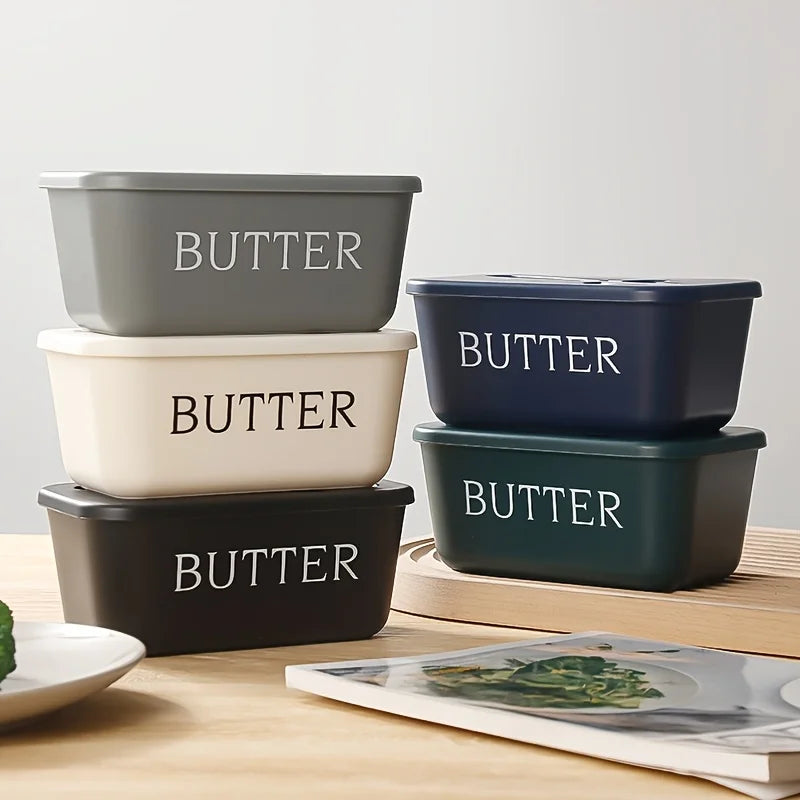 A set of four rectangular storage containers for butter in various shades of gray and blue, resting on a wooden surface.