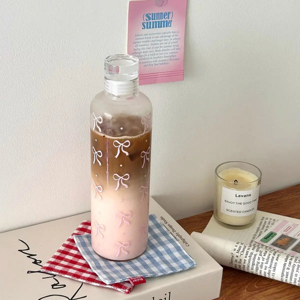 Klare Plastikwasserflasche mit rosa Flüssigkeit und weißen Schleifen auf Holzoberfläche.