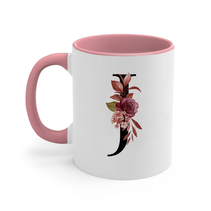 A pink ceramic coffee mug with a black floral monogram design on the side.
