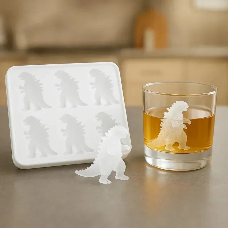 A white silicone dinosaur ice cube tray set with several dinosaur shapes next to a glass of amber liquid.