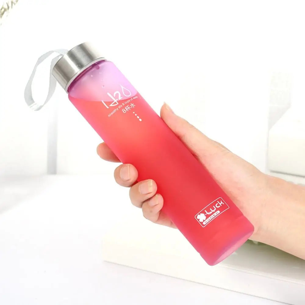A hand holds a pink frosted water bottle with a white loop and a black cap against a white background.