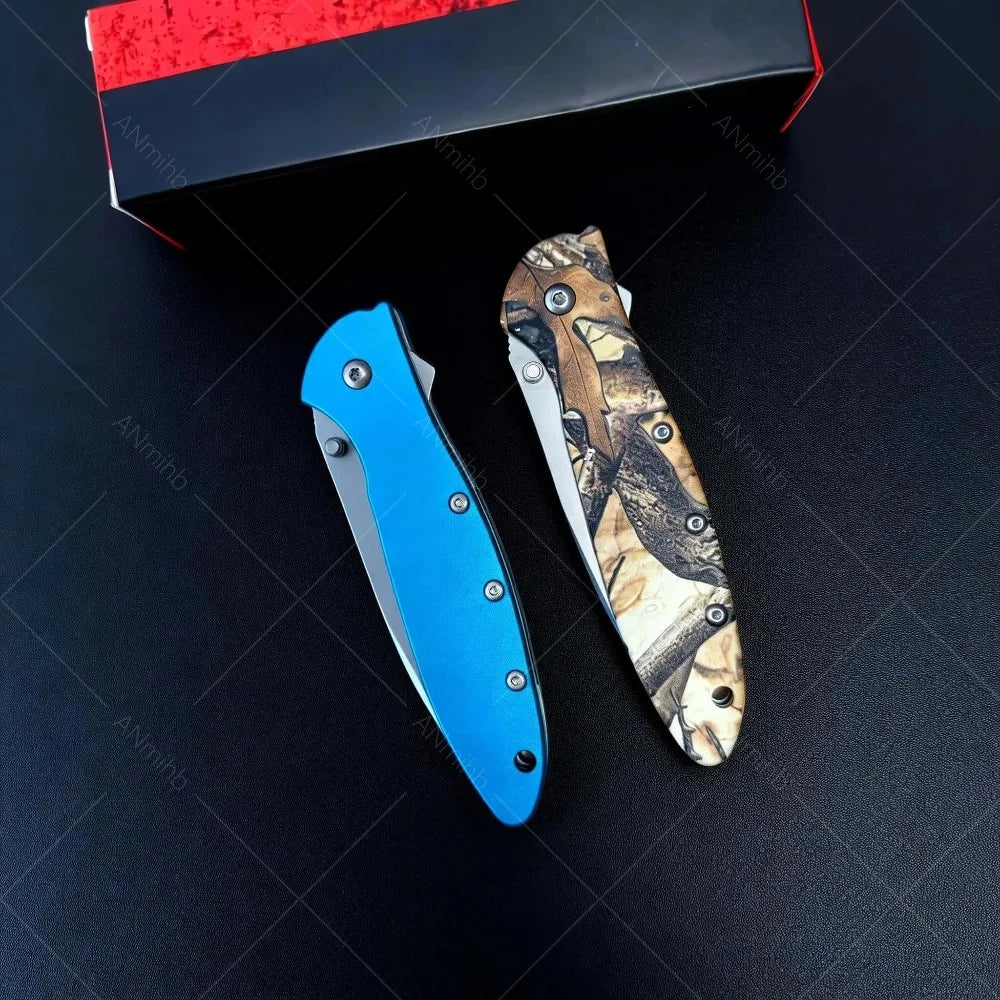 A folding utility knife with a blue blade and a patterned handle is displayed on a dark surface next to its box.