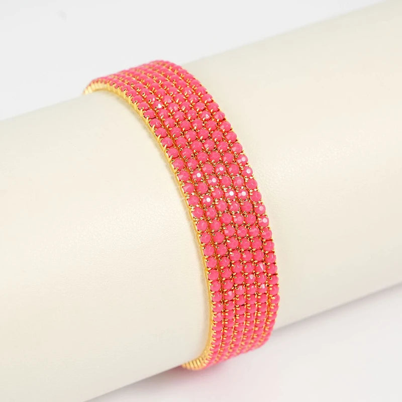 A stack of pink acrylic elastic bracelets with gold accents worn on a wrist.