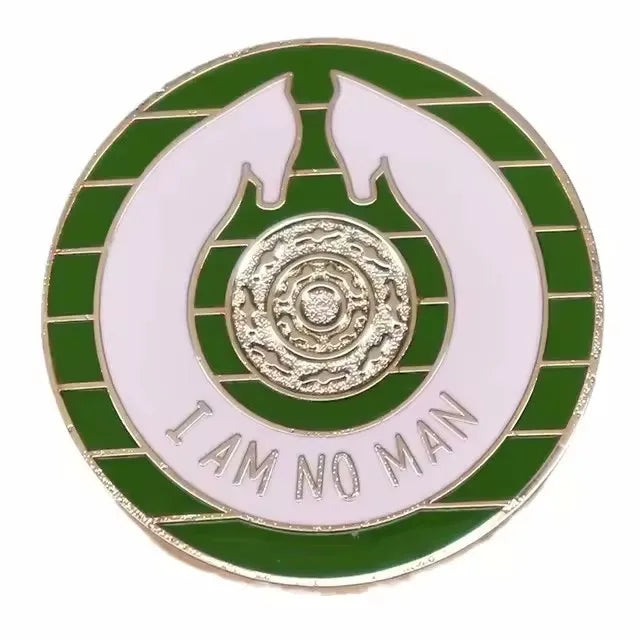 A round enamel pin featuring a gold design on a white background surrounded by green stripes and the text I AM NO MAN
