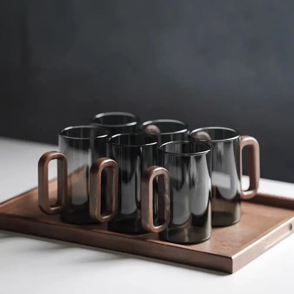 A set of smoke gray glass drinking cups with wood handles resting on a wooden tray.