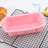 A pink nonstick silicone baking pan with ridges is shown on a black wire rack next to a croissant.