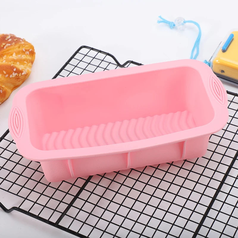 A pink nonstick silicone baking pan with ridges is shown on a black wire rack next to a croissant.