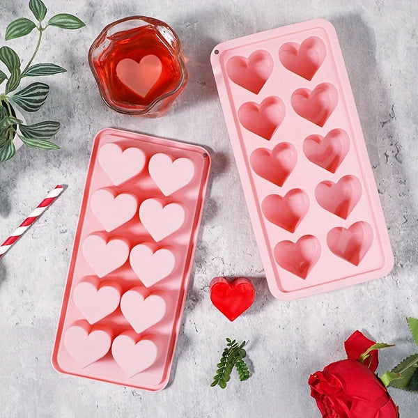Pinkes Silikon-Herz-Eiswürfelform mit roter Flüssigkeit und Rosenblättern auf grauem Untergrund.