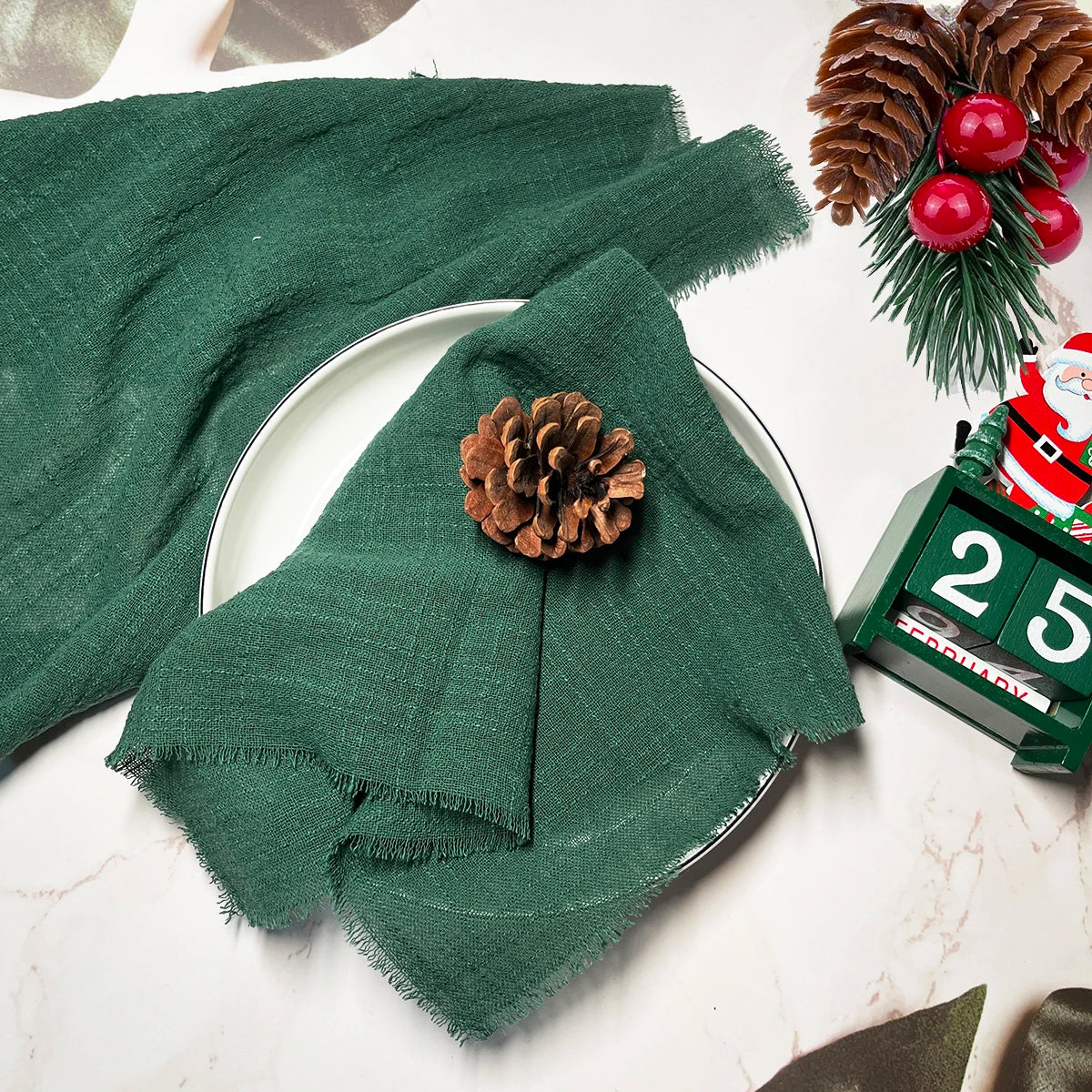 Servilleta de algodón reusable verde oscuro junto a un piña y un reloj navideño.