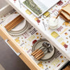 Vista cercana de una estantería de madera forrada con papel estampado, con varios artículos de cocina como platos, palillos y