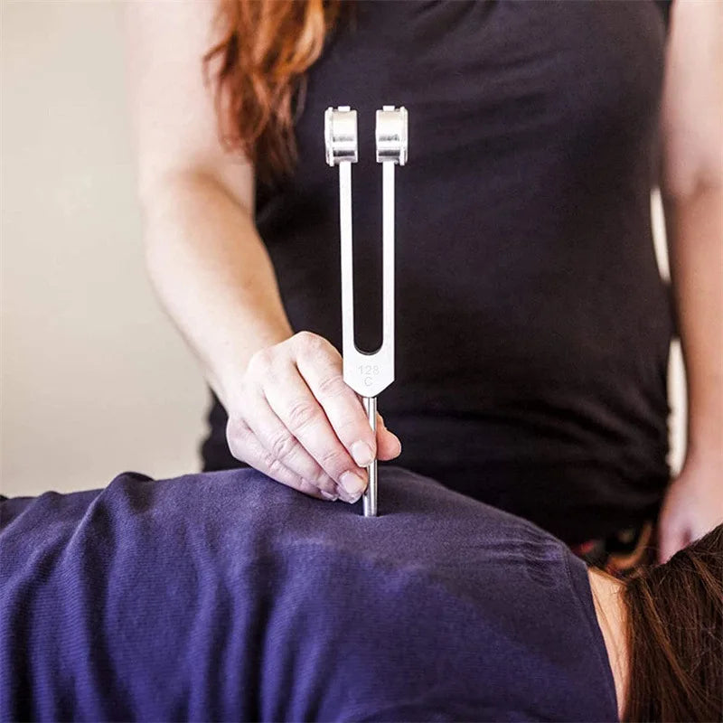 A hand holds a silver tuning fork set against a person's dark shirt.