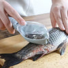 A hand is using a precision fish scale scraper and cleaning brush set to clean a fish on a wooden cutting board.