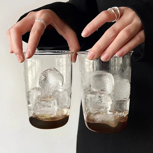Eine Person hält zwei hohe, elegante durchsichtige Gläser gefüllt mit Eis und einer dunklen Flüssigkeit.