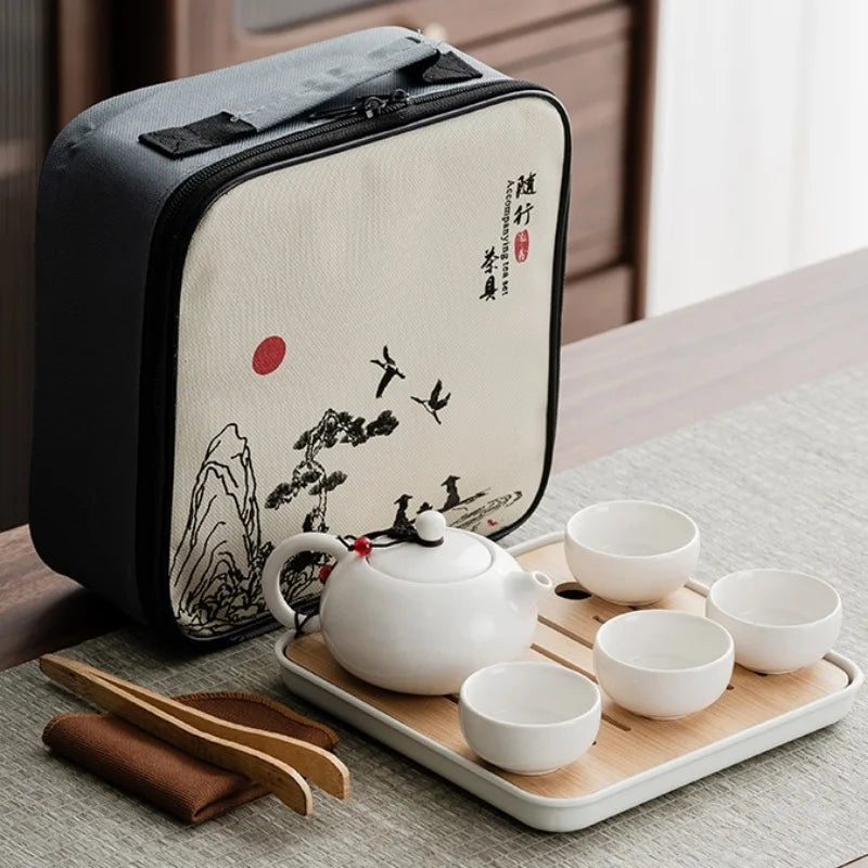 A black carrying case holds an elegant white ceramic tea set with a lid and several small cups on a wooden tray.