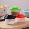 Un set de quatre mini-shakers d'épices avec des couvercles colorés et des contenants blancs, présentés sur une planche en boi