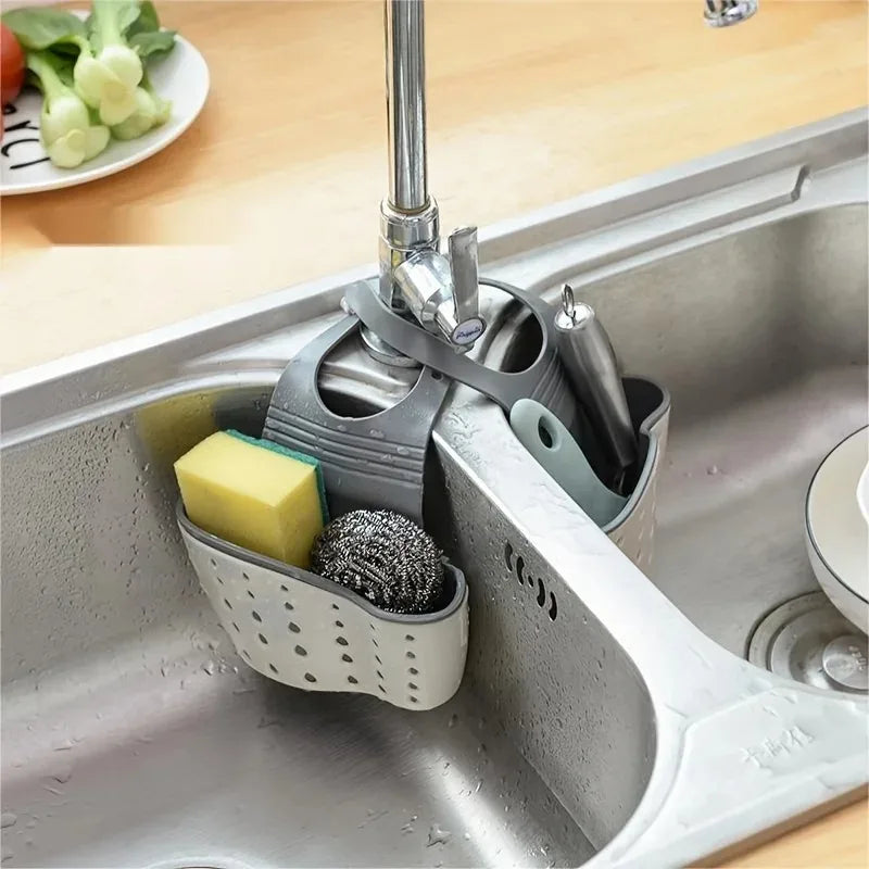 A stainless steel sink drain hanging sponge rack holding a yellow sponge and a black scrubbing brush.