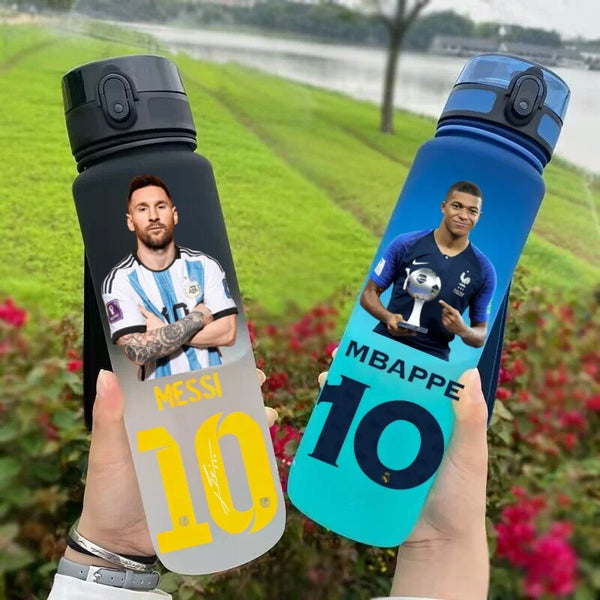Eine Hand hält eine blaue Sportflasche mit einem Fußballspieler und der Nummer 10 vor grünem Outdoor-Hintergrund.