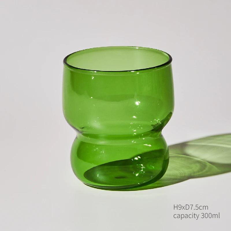 A green glass cup or mug with a rounded body and a thick base, shown against a white background.