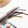 A set of reusable metal drinking straws in various colors and finishes laid on a white surface.