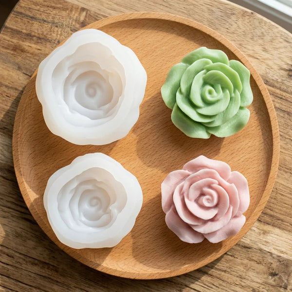A set of three silicone molds shaped like roses in white, green, and pink resting on a wooden board.