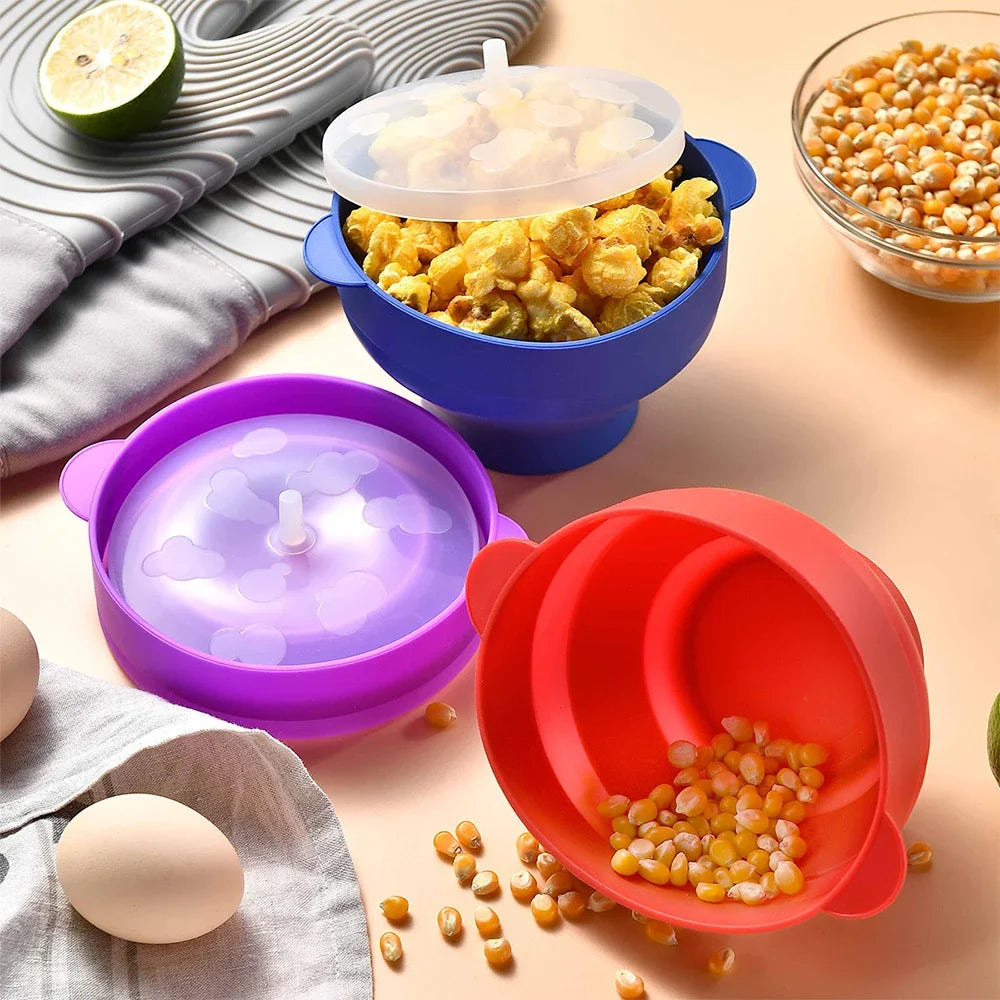 A silicone microwave popcorn bowl set featuring purple and red bowls and a clear lid, with popcorn kernels scattered nearby.