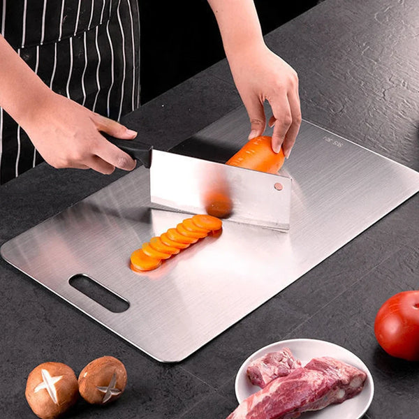 Edelstahl-Cuttingboard mit geschnittenen Karotten und rotem Fleisch auf dunkler Oberfläche