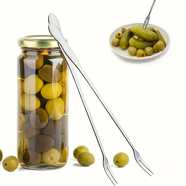 Edelstahlgabelset neben einer Jarre Oliven und Cornichons mit losem grünen Oliven