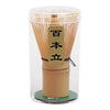 A clear glass container holding a traditional bamboo matcha tea set with a wooden base and a label reading '百本立'.