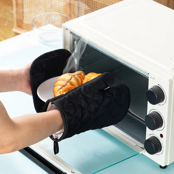 Eine Hand mit schwarzem Ofenhandschuh legt ein gebackenes Stück in einen weißen, schweren Ofen zum Backen.