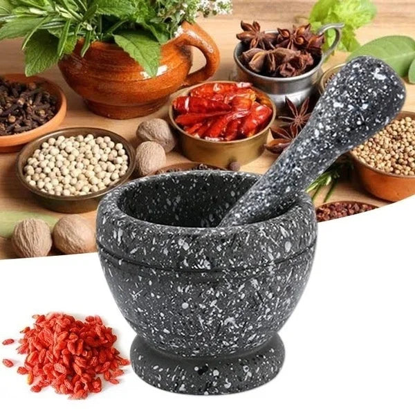 A black stone mortar and pestle set with various dried spices and herbs arranged around it.