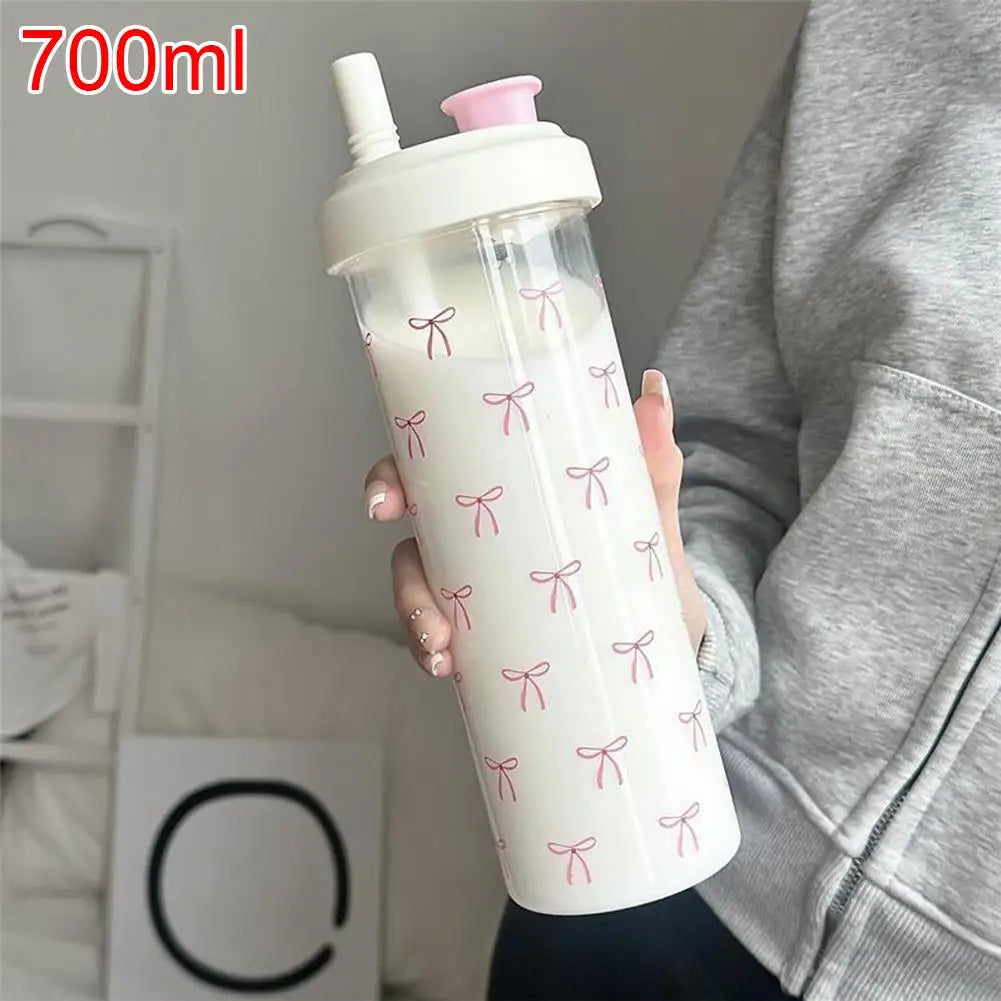 A clear water bottle with a pink lid and decorative pink bows is held by a person.
