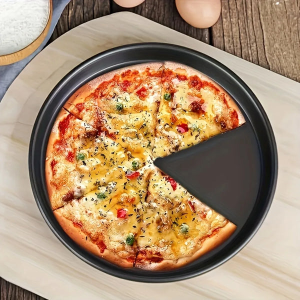 A slice of pizza is served in a black carbon steel nonstick pizza pan on a wooden surface.