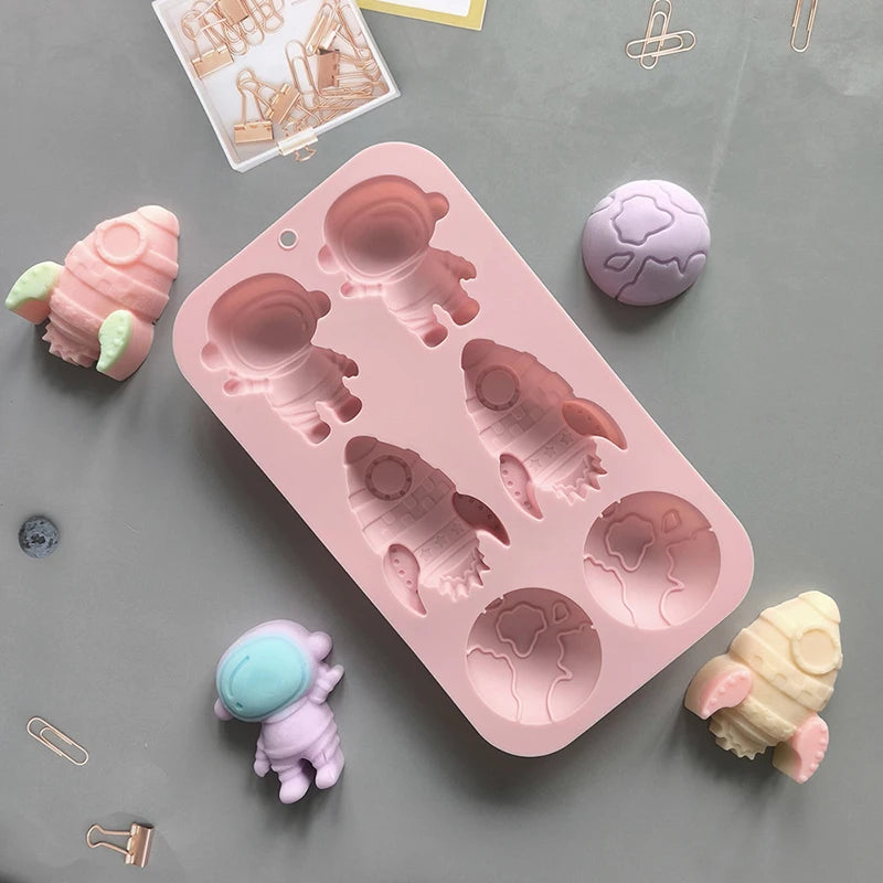 A pink silicone mold with six astronaut rocket shapes is displayed on a gray surface.