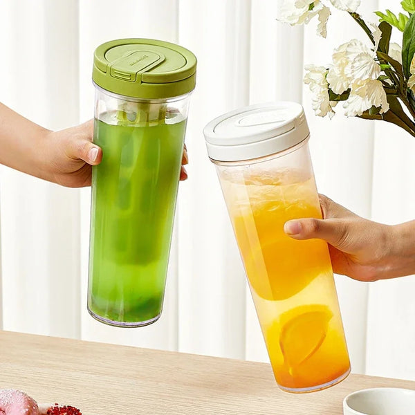 Hände halten eine klare Flasche mit grünem Flüssigkeit und eine orangefarbene Flasche, beide mit hellgrünen Deckeln.