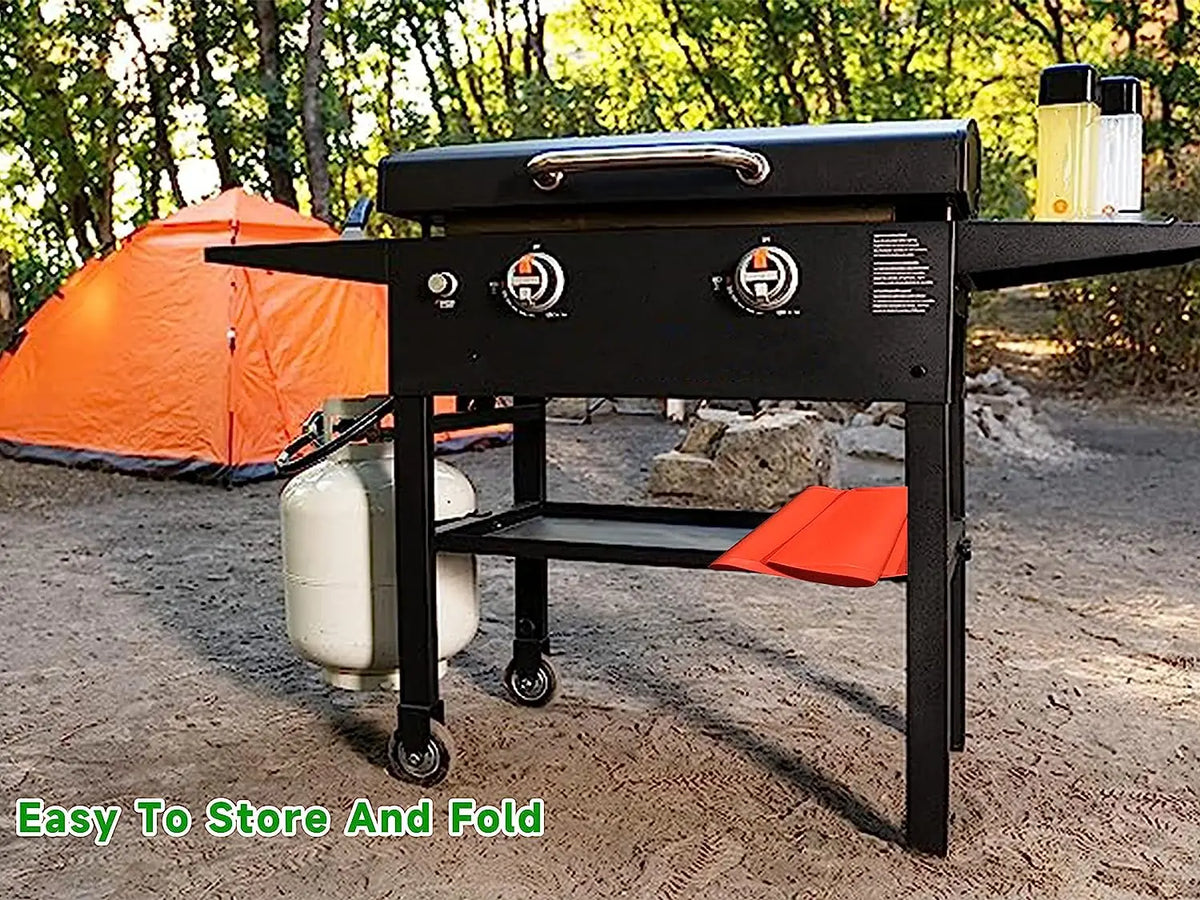 A black silicone BBQ baking mat is shown outdoors on a wooden stand with orange accents.