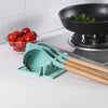 A teal silicone utensil drying rack organizer with wooden handles is placed on a white countertop next to fresh tomatoes.