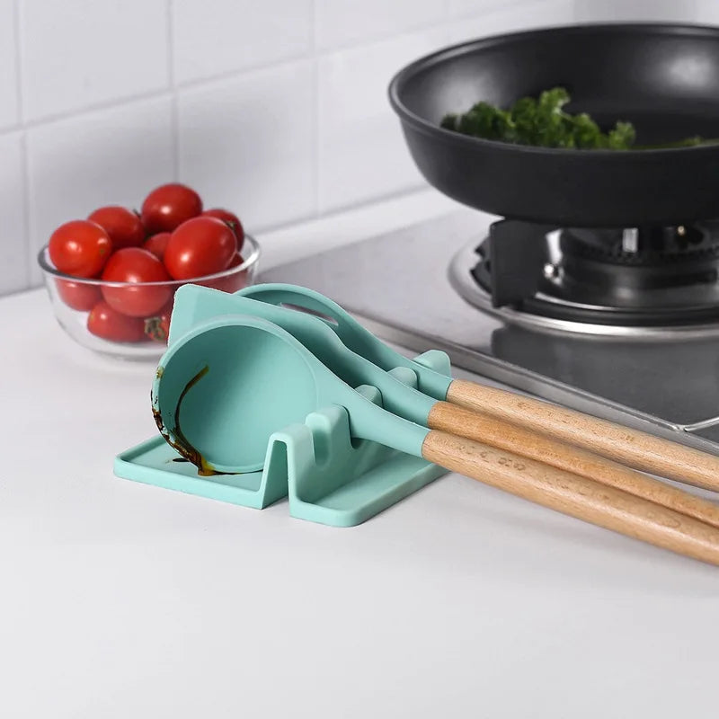 A teal silicone utensil drying rack organizer with wooden handles is placed on a white countertop next to fresh tomatoes.