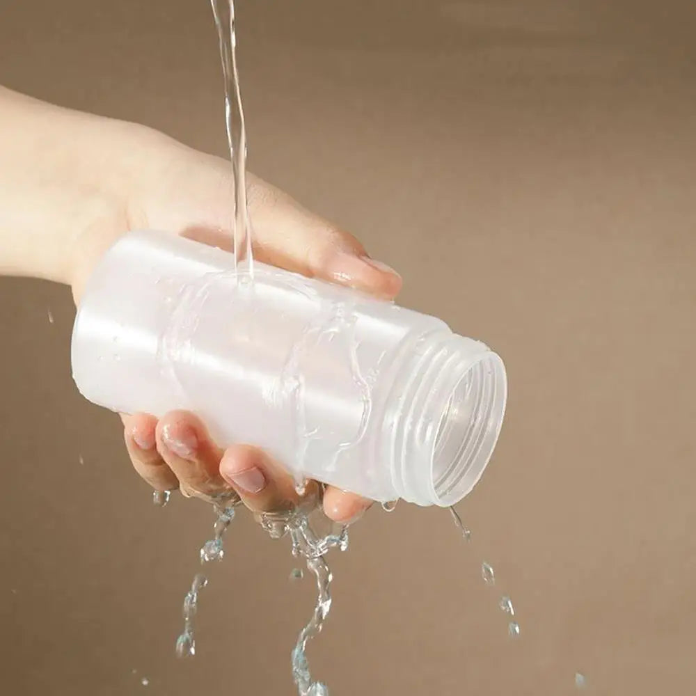 A hand is squeezing a clear plastic bottle, causing liquid to drip out.