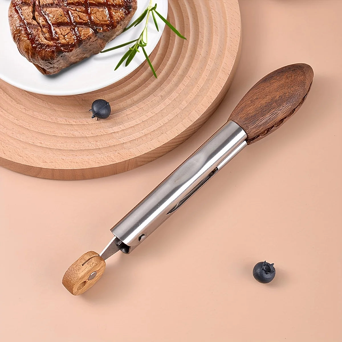 A pair of walnut wood kitchen tongs with a stainless steel head and hanging loop resting on a light beige surface next to a p
