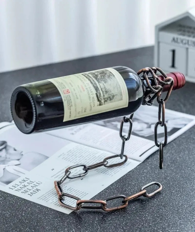 A dark glass bottle of wine is suspended by a metal chain, resting on a sheet of paper.