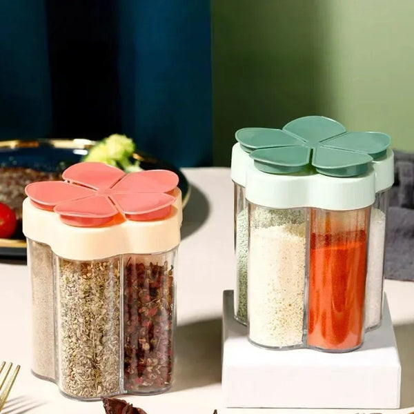 A clear multi-opening seasoning jar with green and pink lids filled with various spices on a white surface.