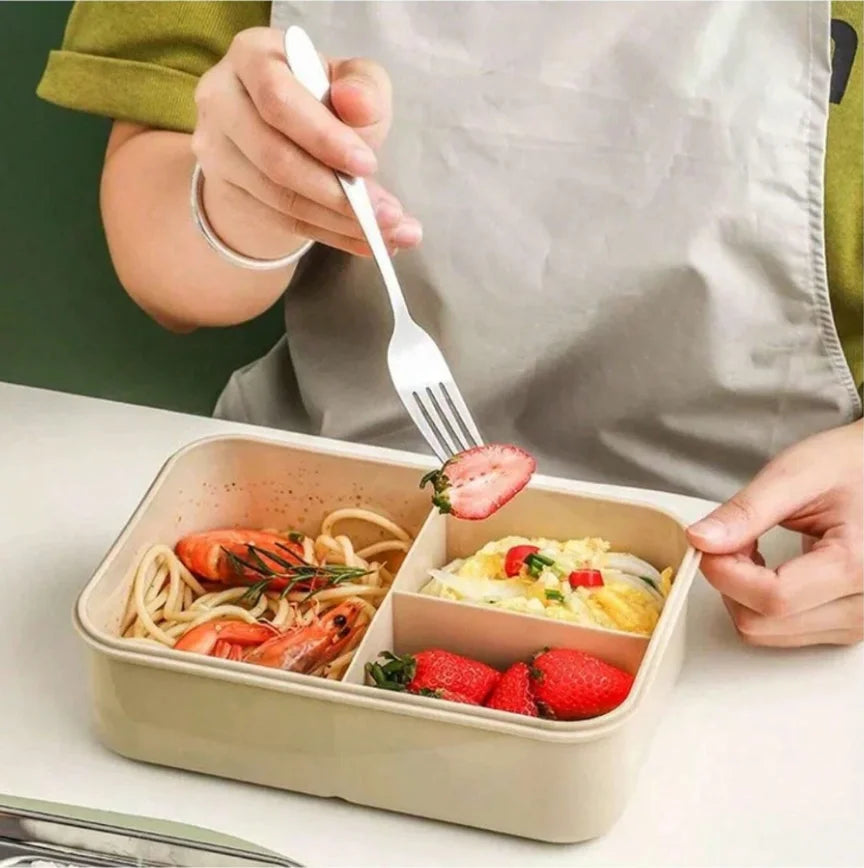 A person is using a fork to serve food from a beige 3-compartment adult bento box set filled with pasta and strawberries.