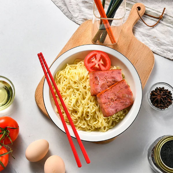 Eine Schale Nudeln mit Streifen rosa Fleisch und Chopsticks auf einem Holzbrett.