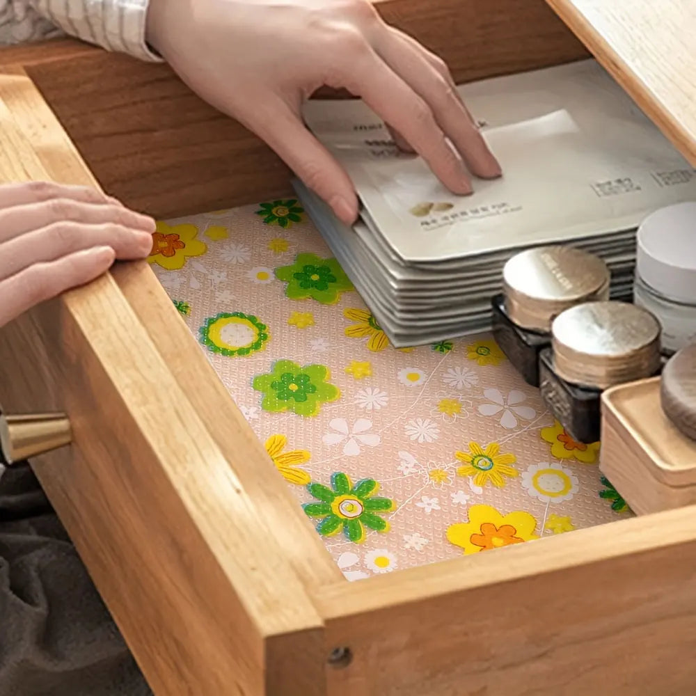 Una mano coloca una pila de protectores de estantes blancos en un gabinete de madera con un forro estampado floral visible.