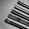 Five pairs of black chopsticks with gold accents arranged diagonally on a gray surface.